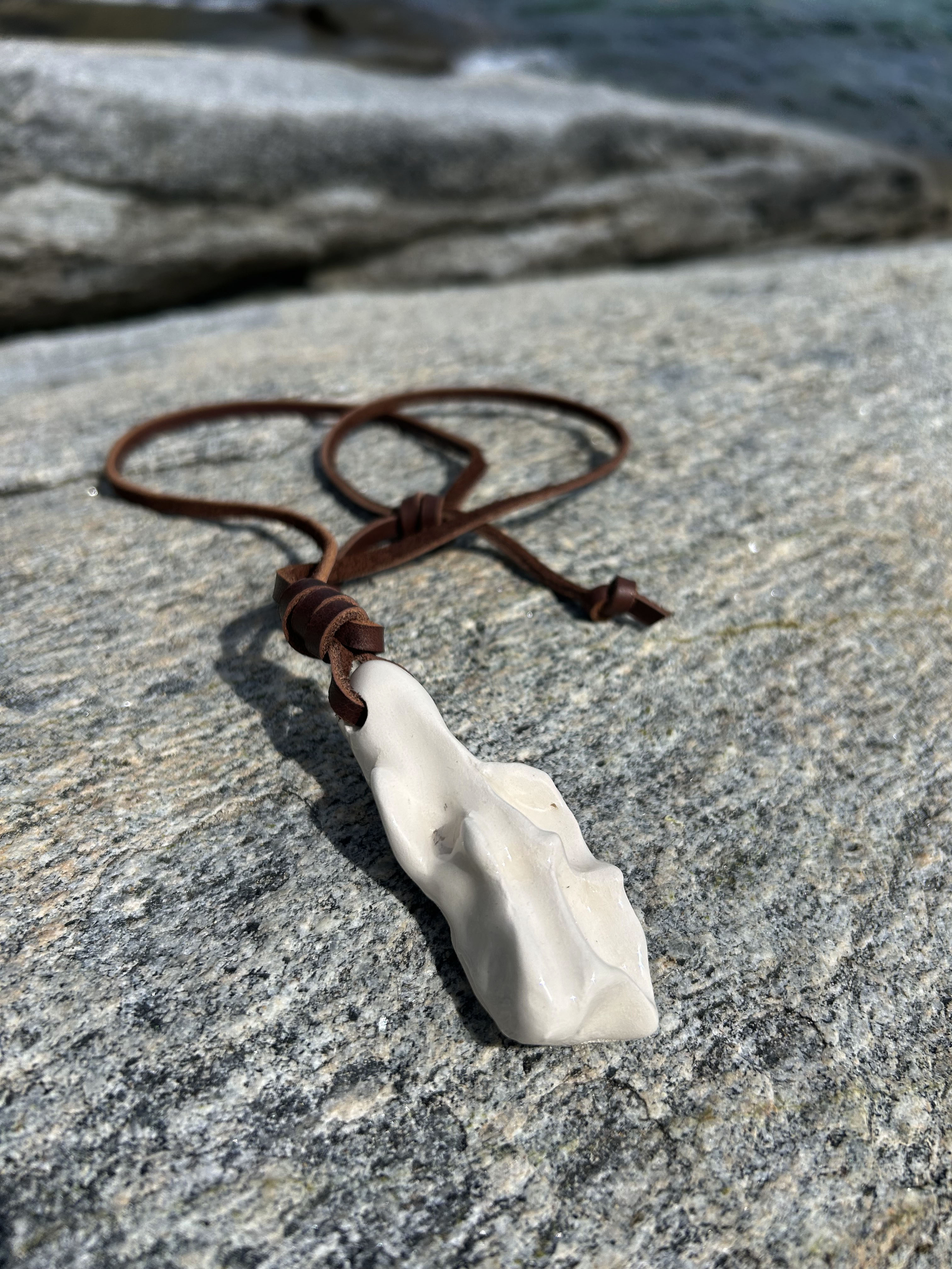 Second view of ceramic pendant with leather cord on rock