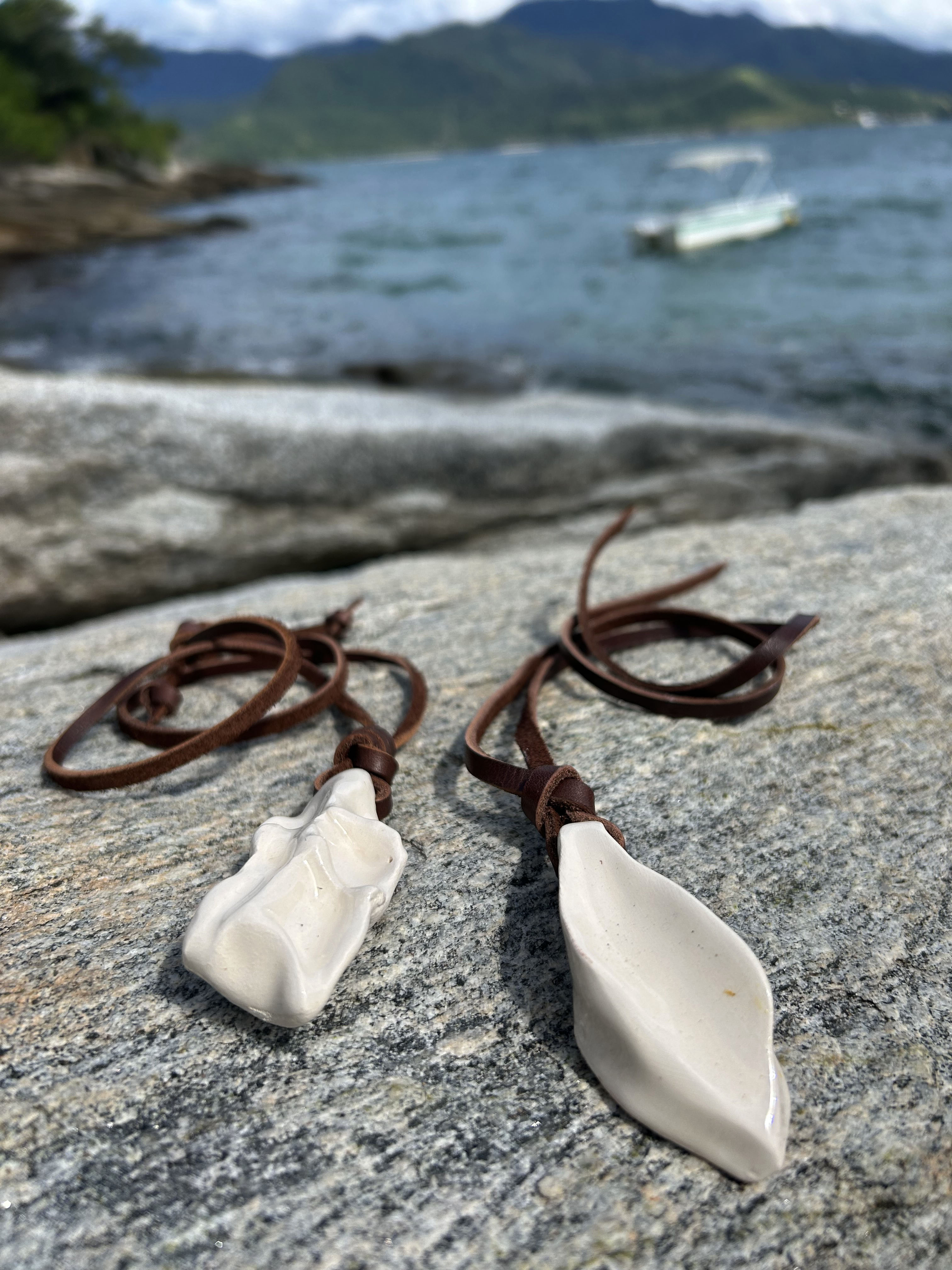 Two ceramic pendants on leather cords with sea in the background