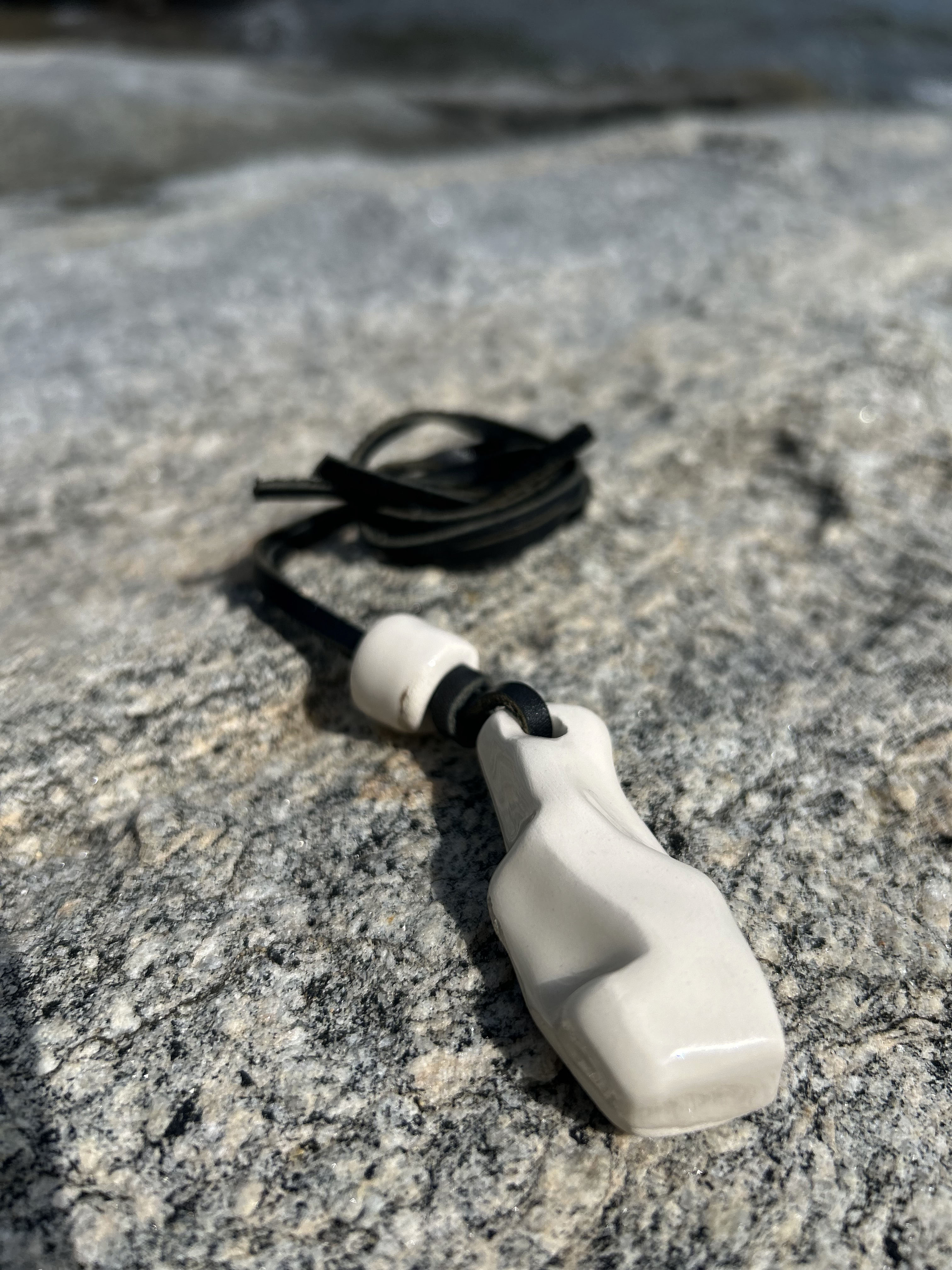 Ceramic pendant on black cord on rock surface